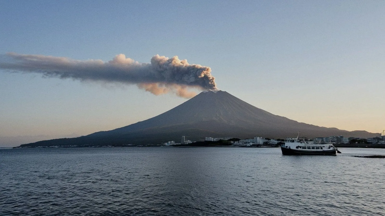 夕陽下櫻島火山矗立於鹿兒島灣，山頂飄著淡白色煙霧
