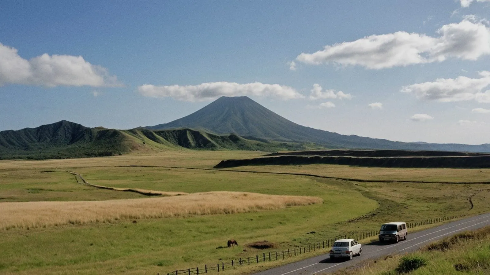 阿蘇草原金綠色草地延伸至遠方，馬兒悠閒吃草，阿蘇火山冒著白煙